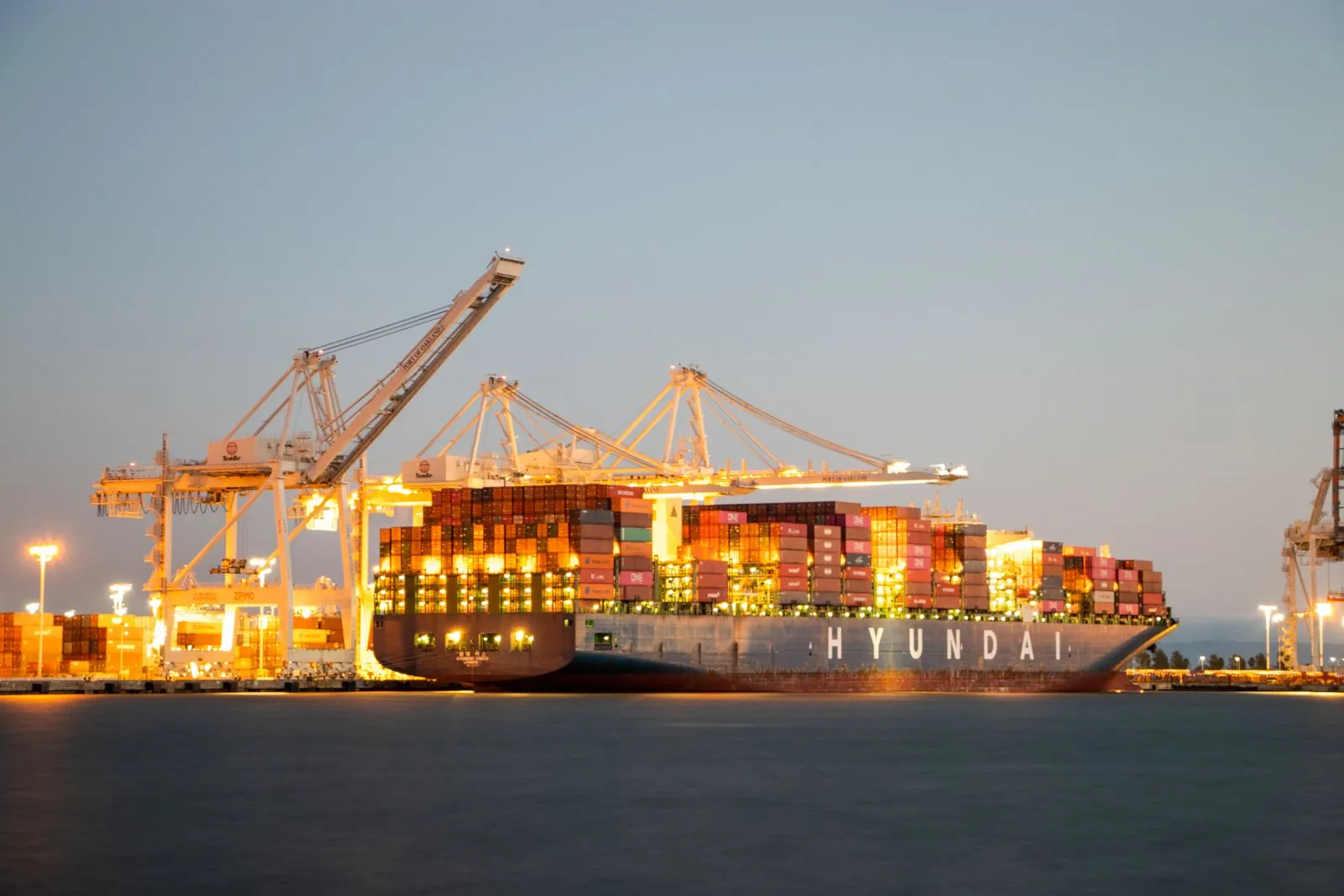Container ship docked under illuminated cranes at twilight