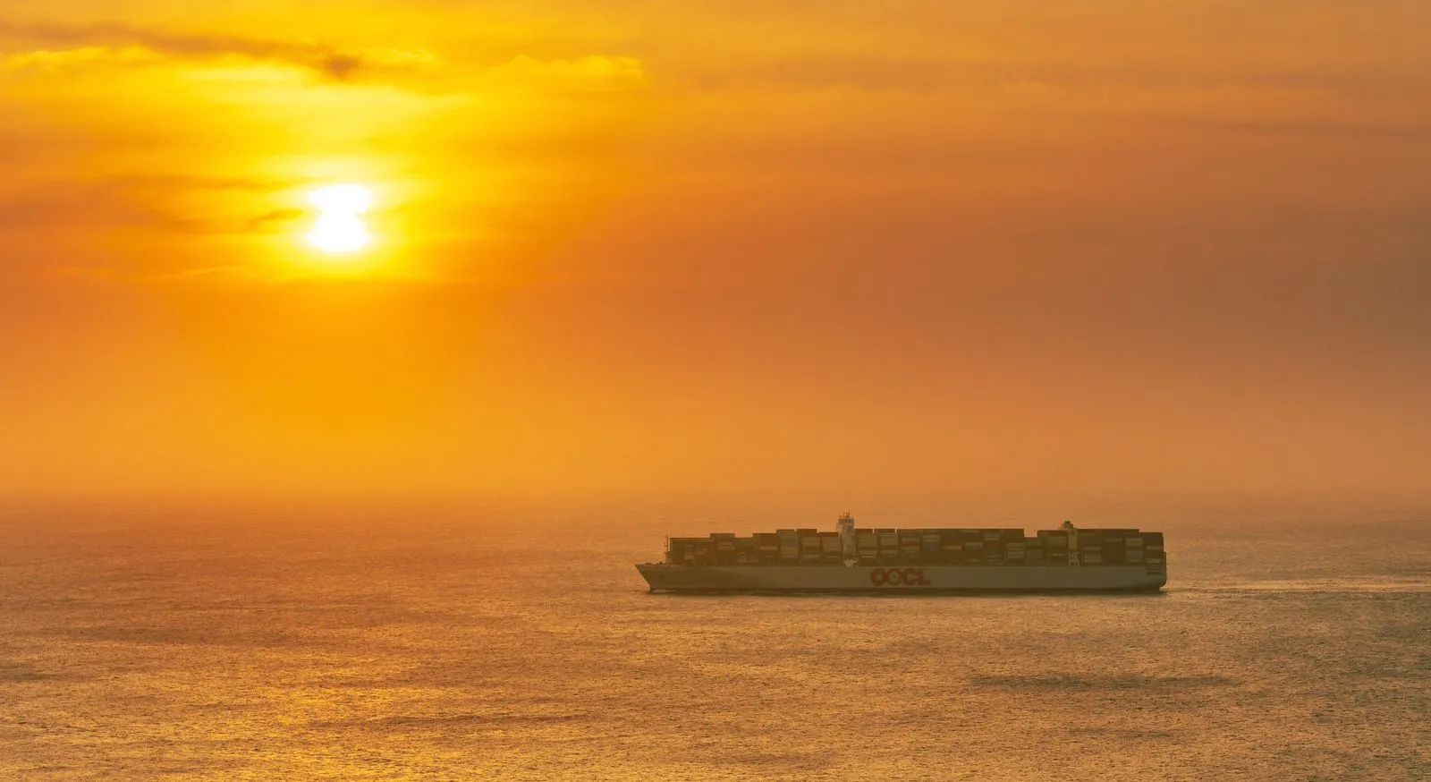 Container ship crossing a calm sea under an orange sunset